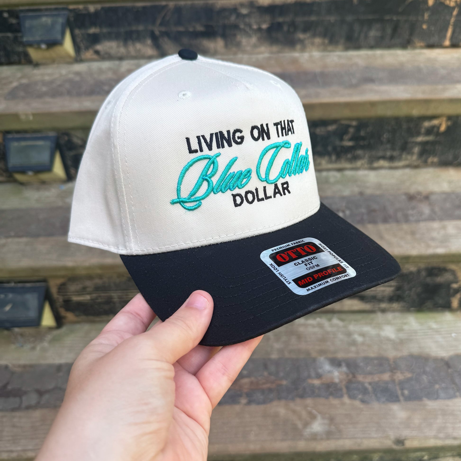 Cap with 'Living on That Blue Collar Dollar' text held by a hand against a wooden background