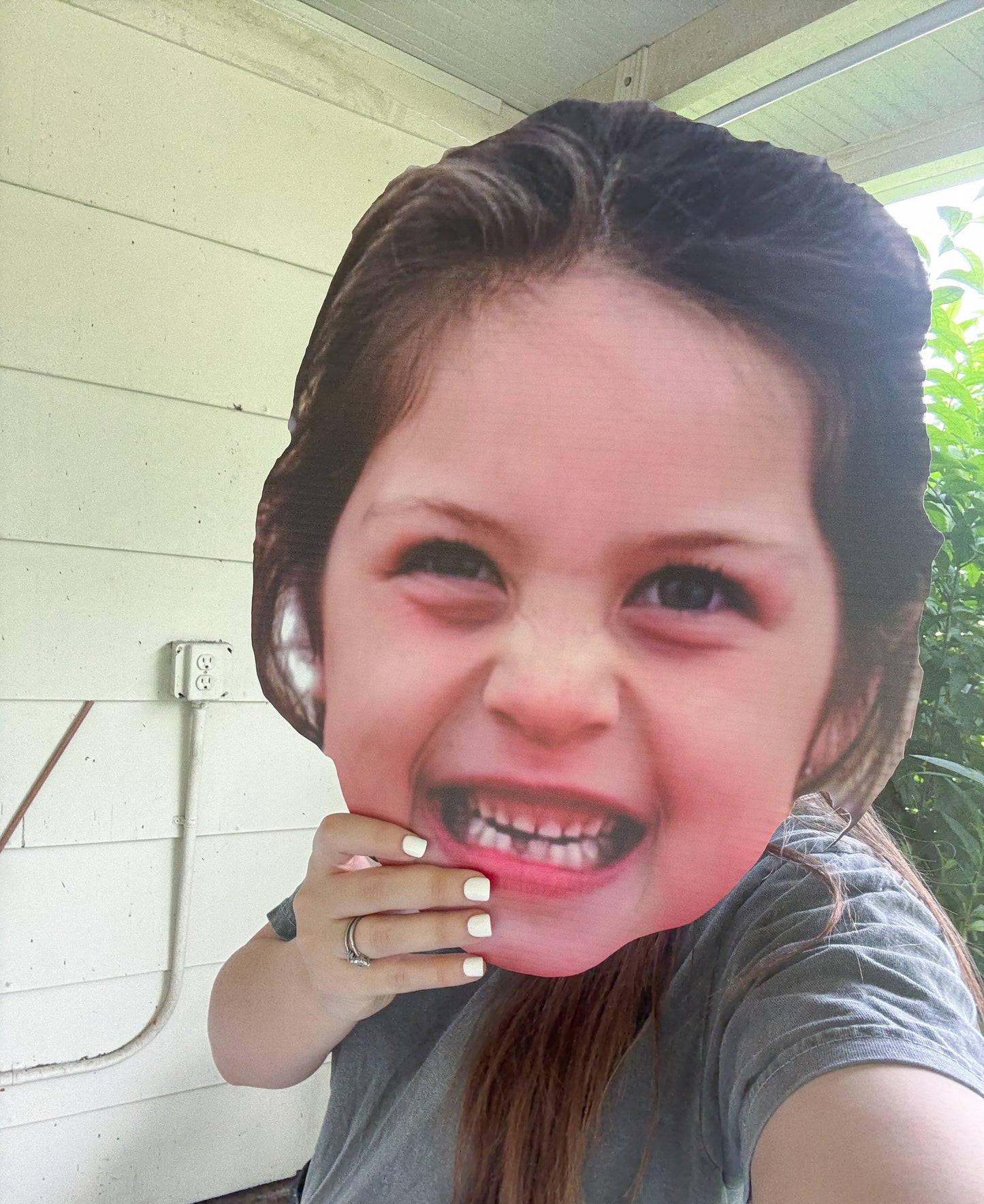 Person wearing a cardboard cutout of a smiling face outdoors.