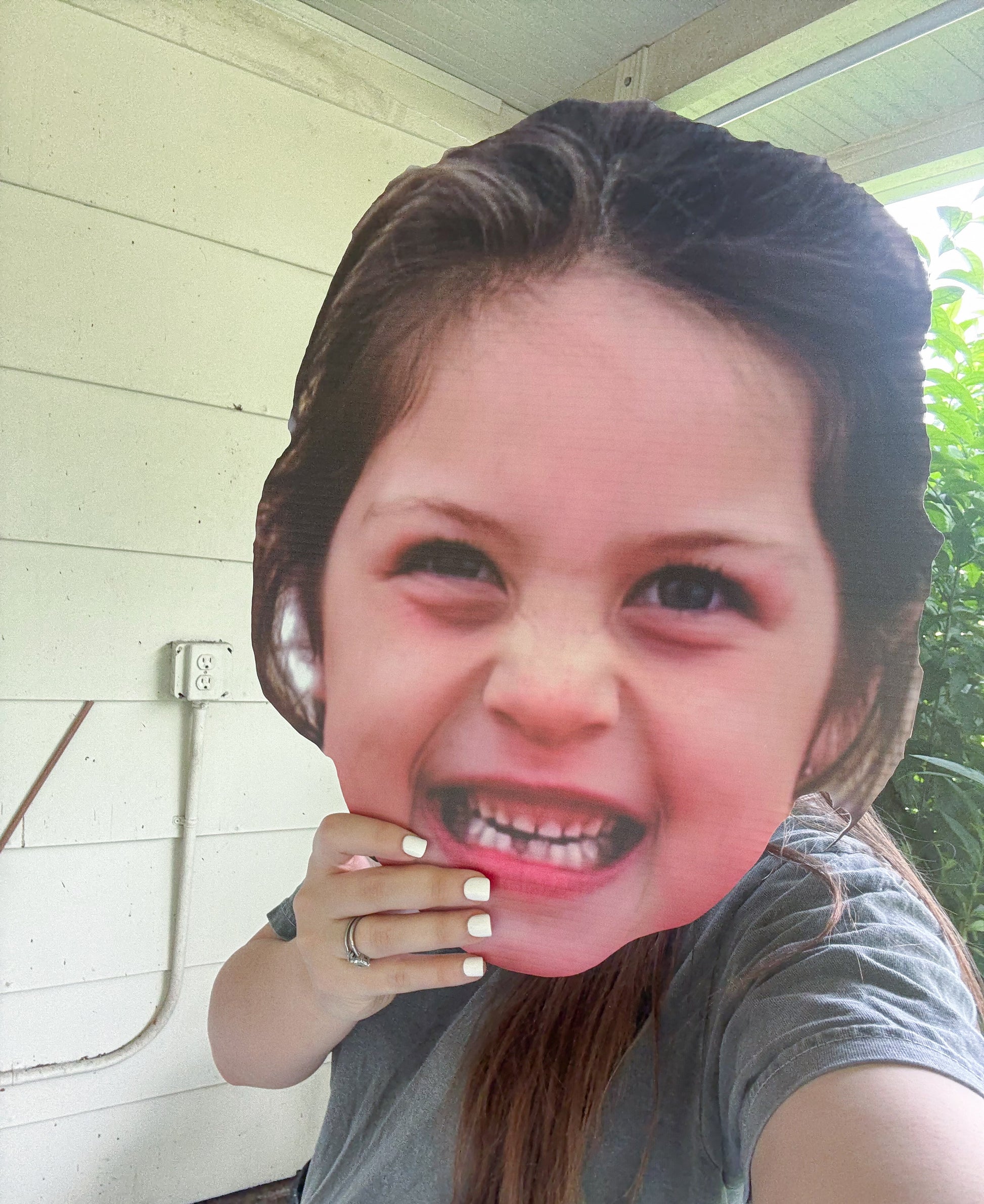 Person wearing a cardboard cutout of a smiling face outdoors.
